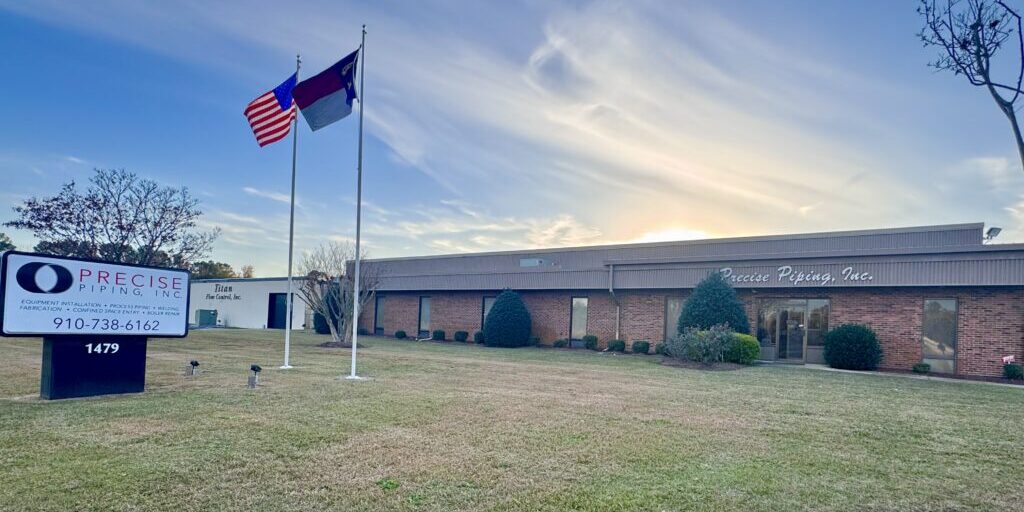 American and state flags flying outside a large brick building under a bright sky.